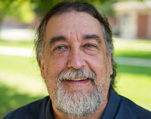 Man in navy blue shirt standing in front of grass.