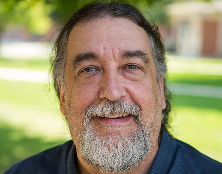 Man in navy blue shirt standing in front of grass.