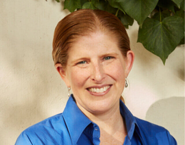 portrait of a smiling woman with red hair, wearing a blue button-up blouse