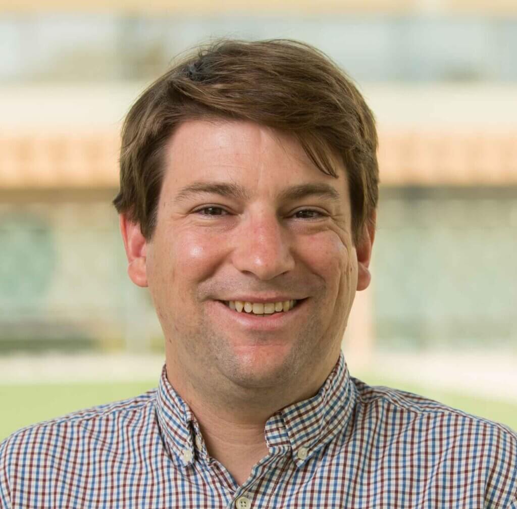 a man with short brown hair and a brown and blue striped shirt smiles at the camera
