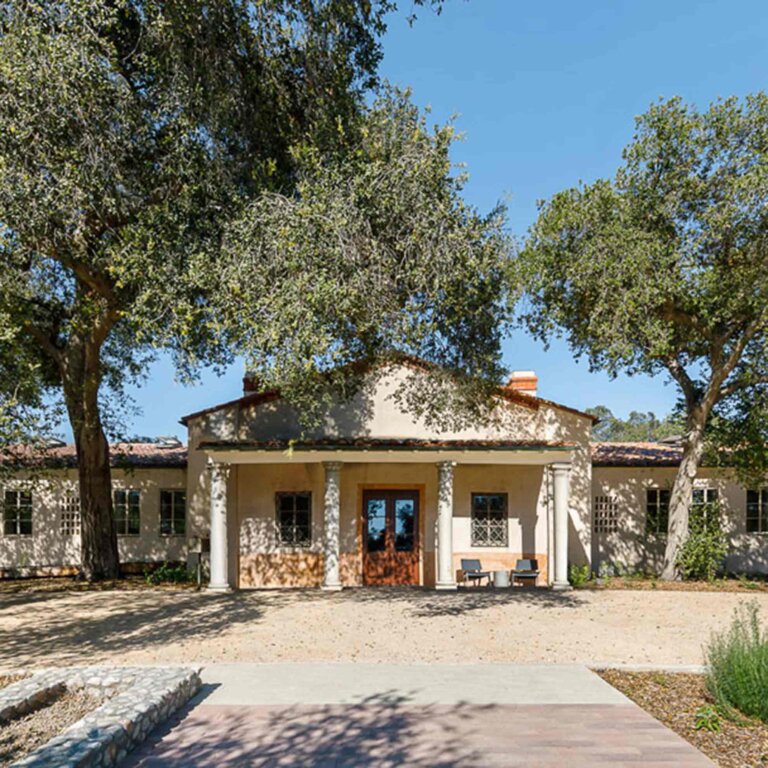 a white building with roman columns surrouded by oak trees