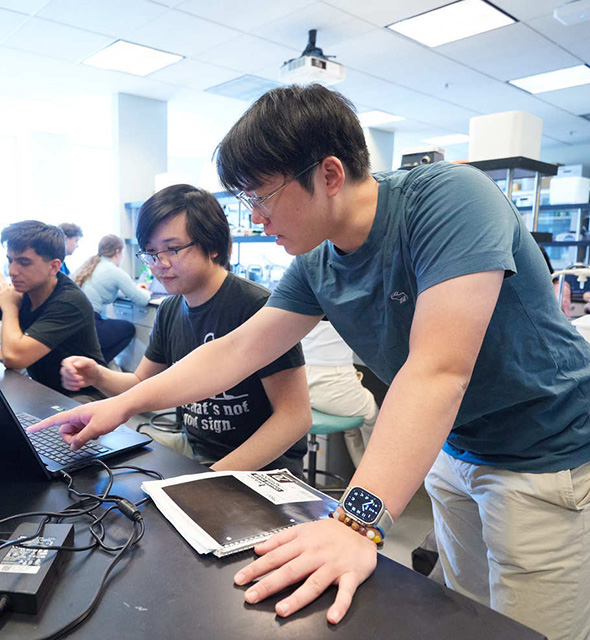 A student shows his labmate some information on a laptop
