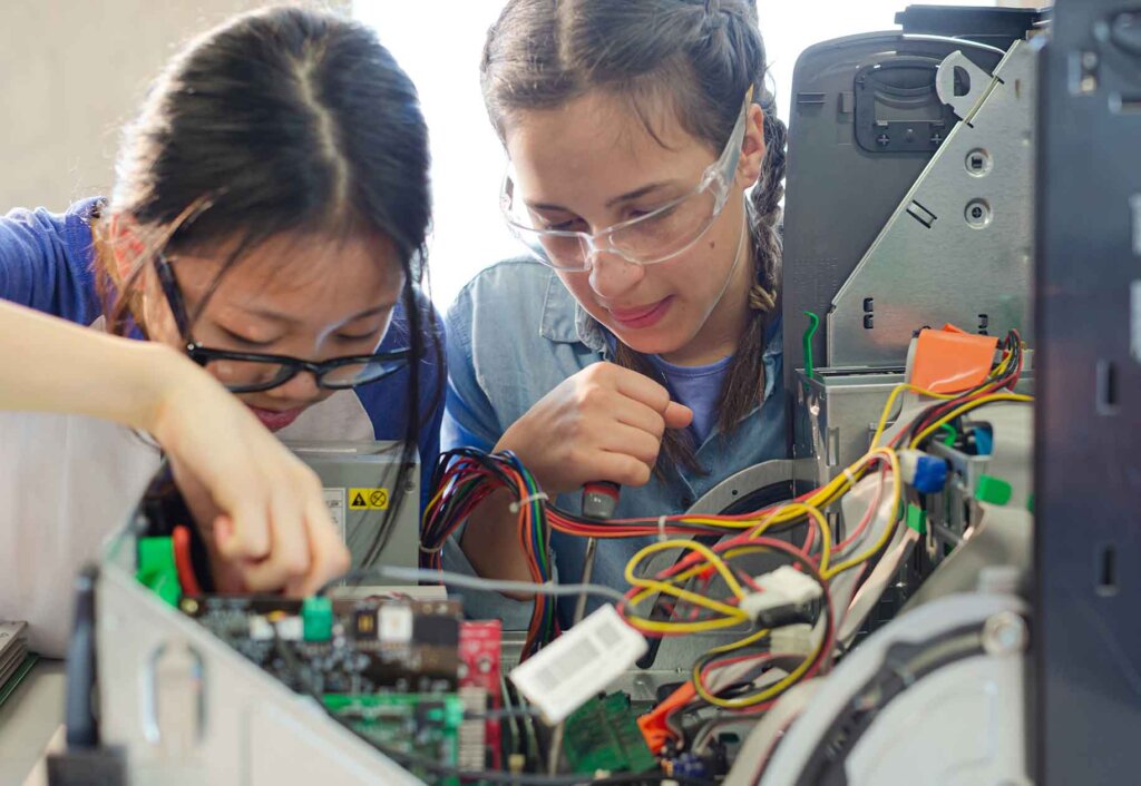 two women work on the the inside electronics of a machine
