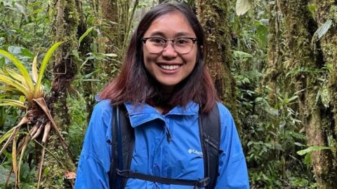 Chanchanok wears a blue windbreaker and backpack while in a jungle in Thailand