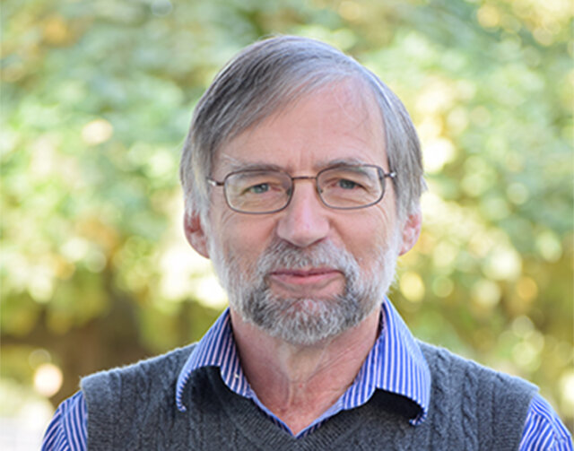 Man in short white hair wearing glasses and a grey vest.