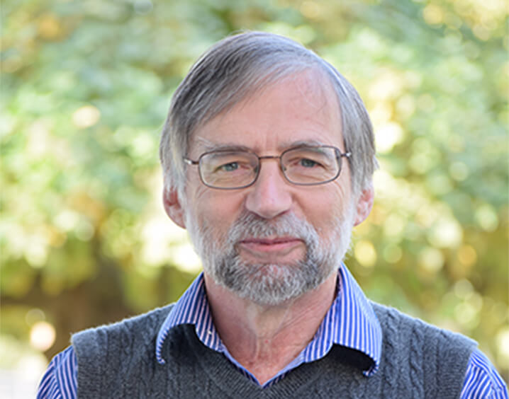 Man in short white hair wearing glasses and a grey vest.