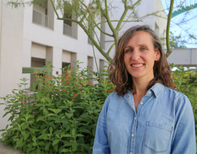 Woman with short light brown hair and blue long sleeve button up.