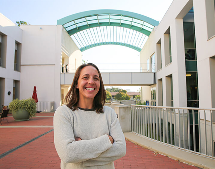 Woman with short light brown hair in white long sleeve sweater in front of buidling.