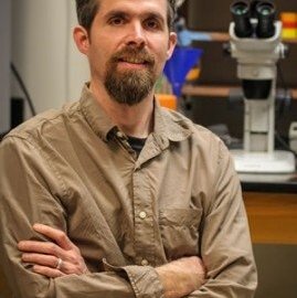 Patrick Ferree poses in front of a microscope