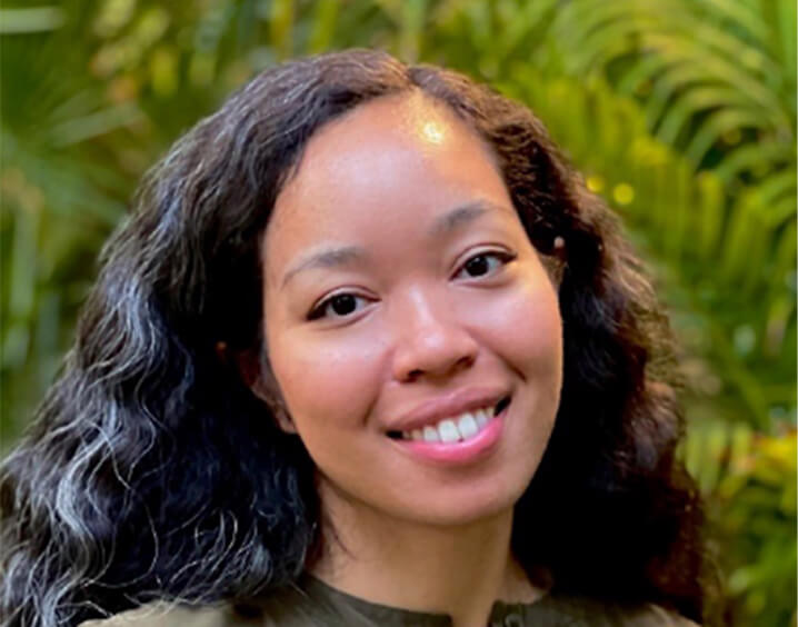 Woman with long black curly hair in front of bushes.