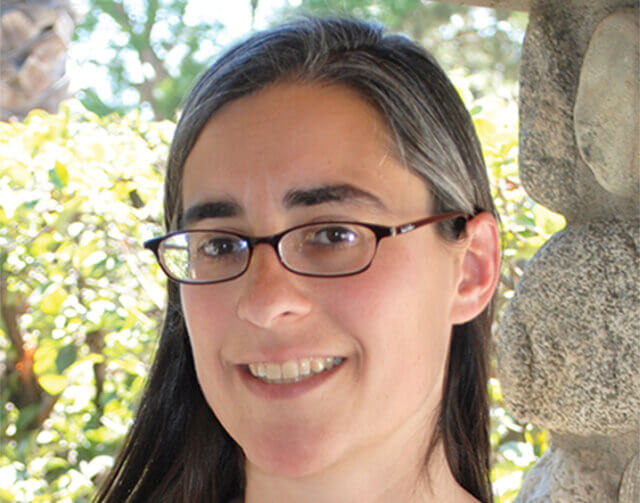 Woman in black long hair and glasses smiling.