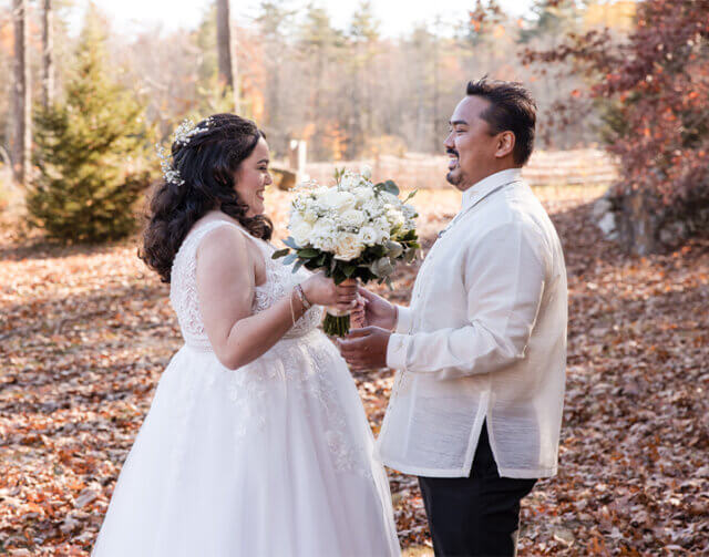 Woman in wedding dress holding bouquet of flowers looing at man in white shirt and black pants.