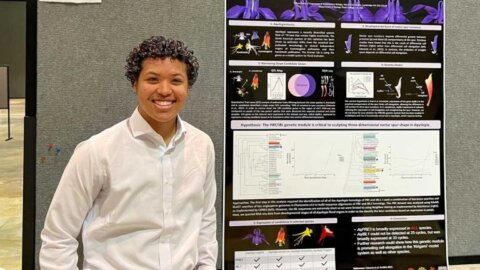 Teo Cooper poses in front of their poster presentation