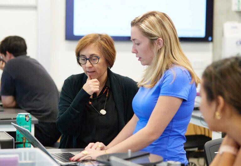a professor and student work together on a laptop in a classroom