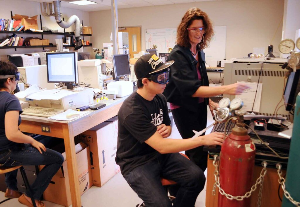 a student and professor work together at a machine in a lab