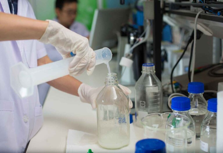 close up of hands pouring chemicals from a beaker into a glass bottle.