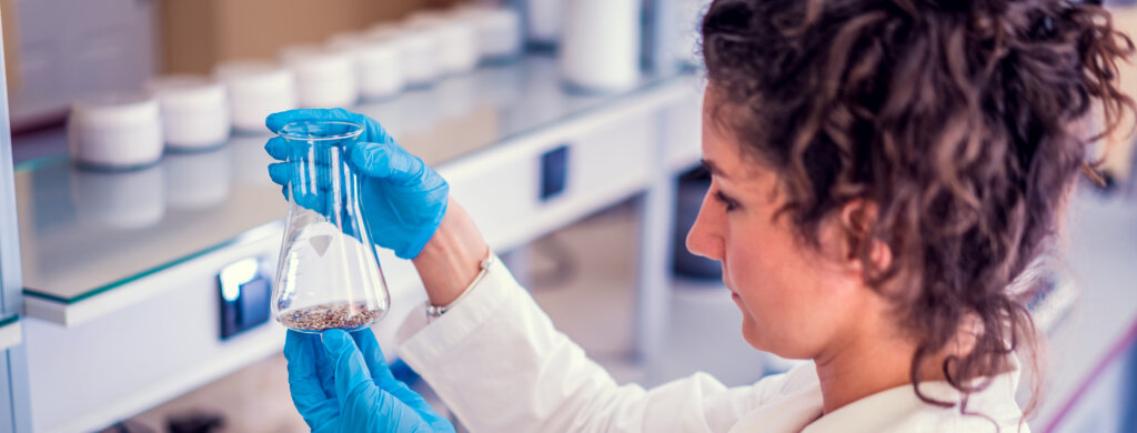 A woman in a lab coat examines the contents of a flask