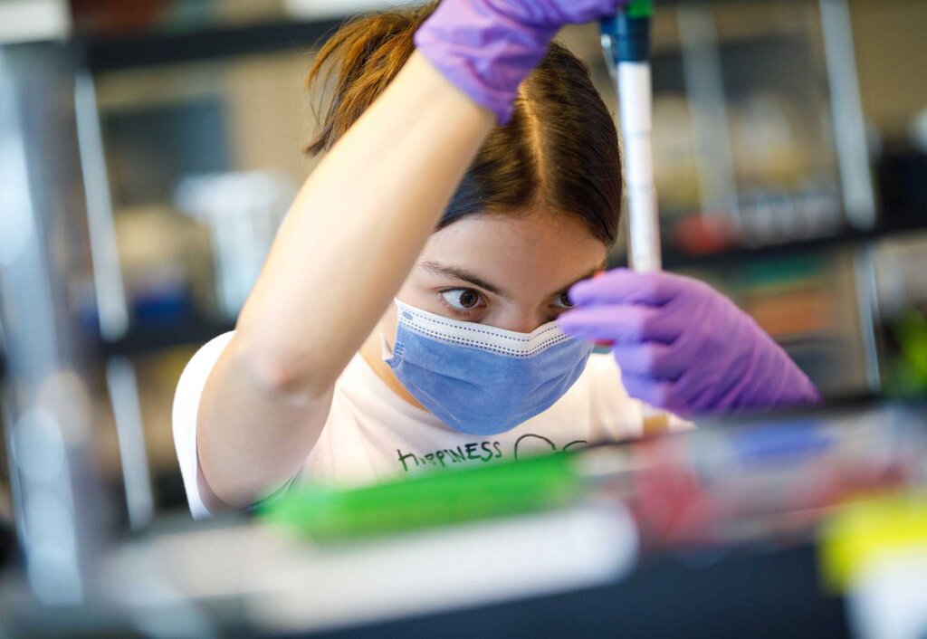 a student wearing a mask measures out liquids into a vial.