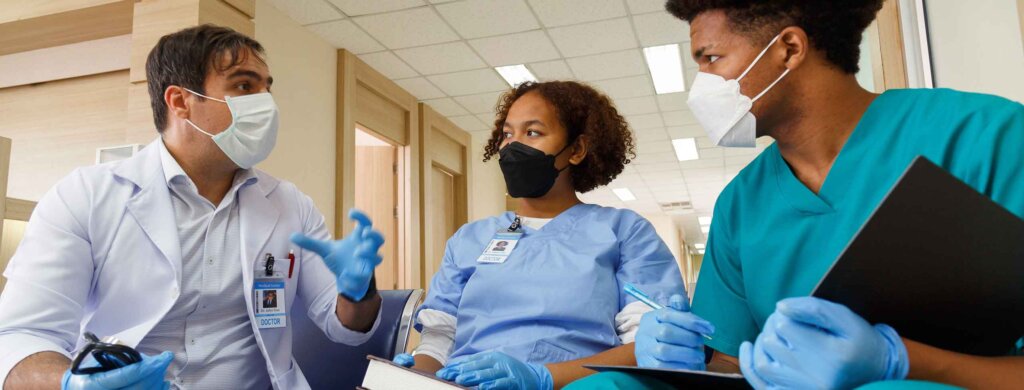 two students wearing masks are instructed by a doctor in a clinical setting
