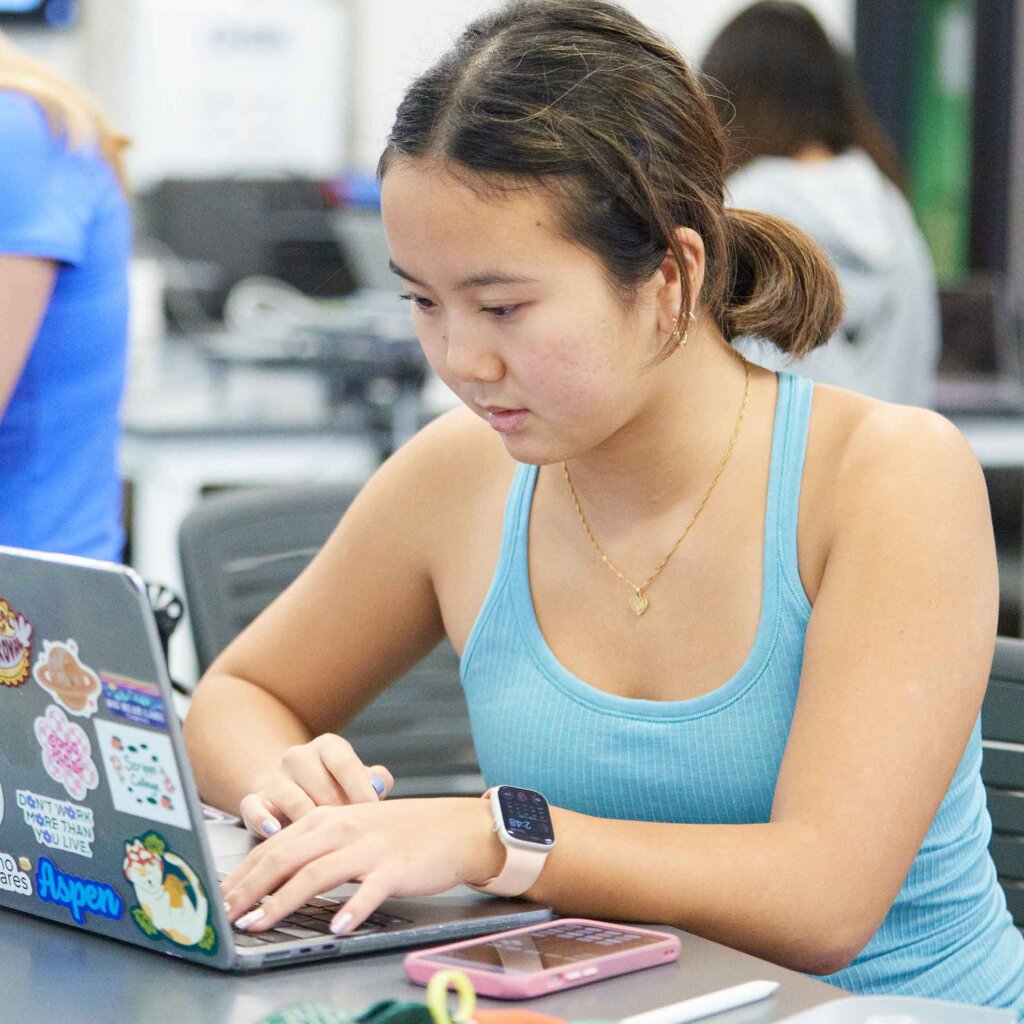 a student wearing a tanktop works at a laptop in a lab