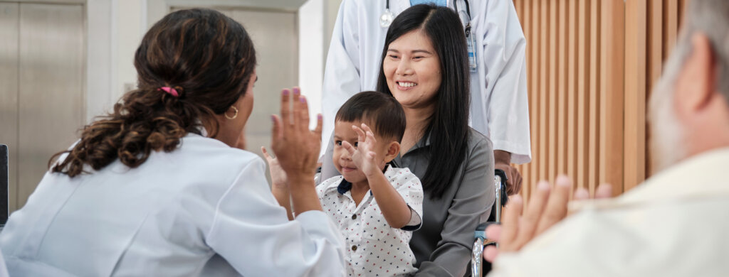 A doctor high fives a child sitting in his mother's lap