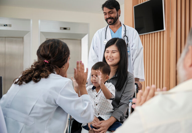 A doctor high-fives a child sitting in his mother's lap
