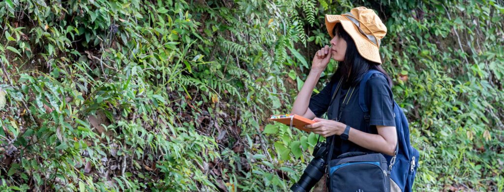 a student wearing a safari hat smells a leaf from the surrounding environment