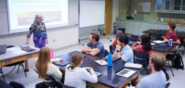 a group of students sit in desks while listening to a professor give a lecture