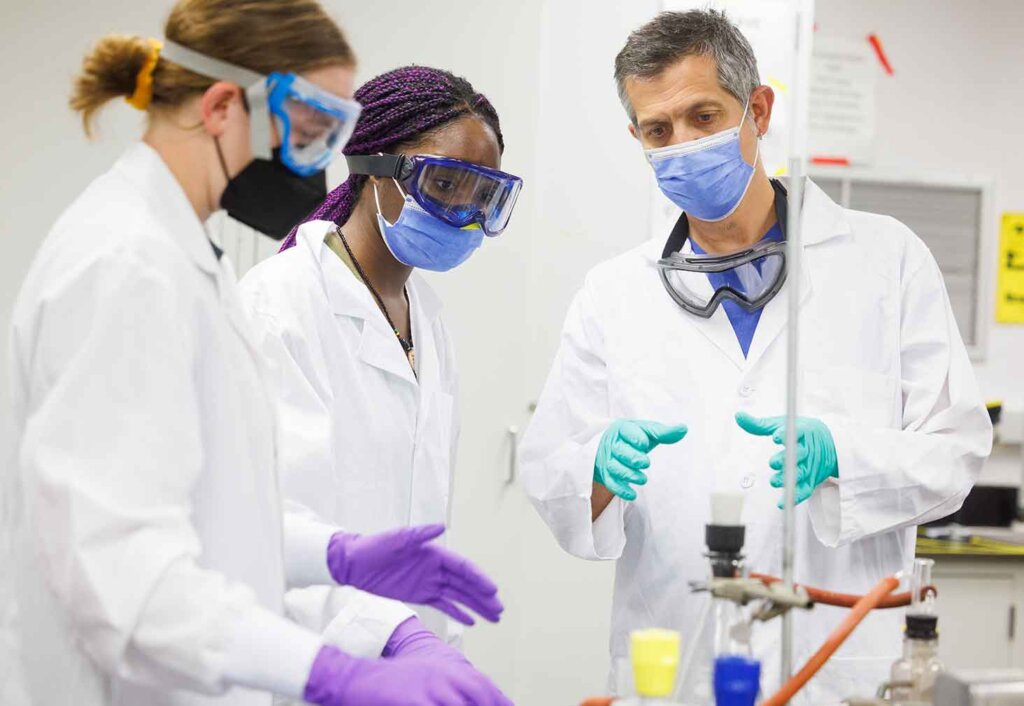 two students work with a professor in a lab