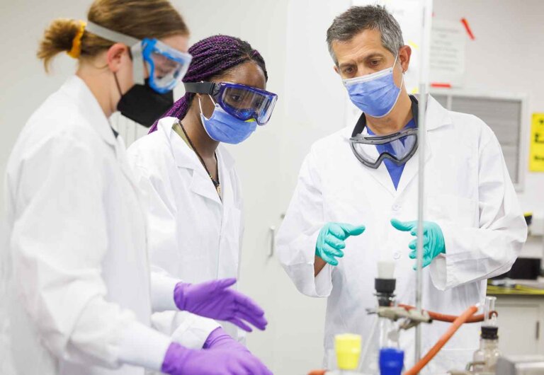 two students work with a professor in a lab