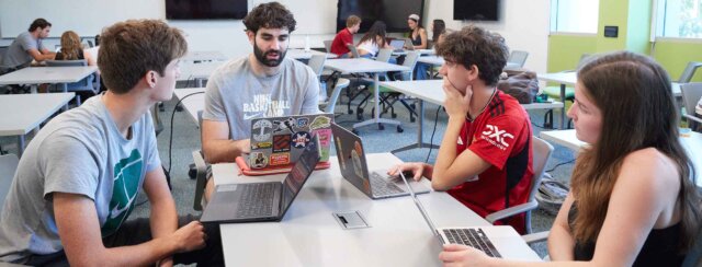 four students doe group work at a large table in a classroom