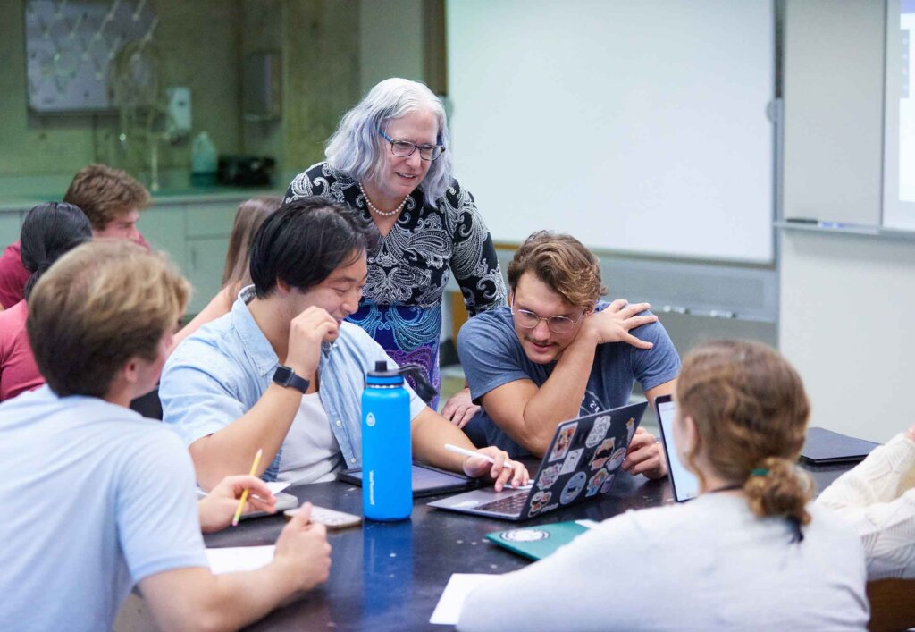 a professor talks to a group of students sitting a large table