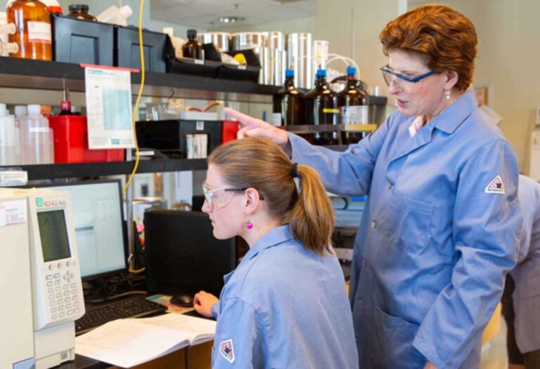 a student and professor work together at a machine in a lab