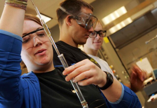 three students work in a lab measuring liquids into vials