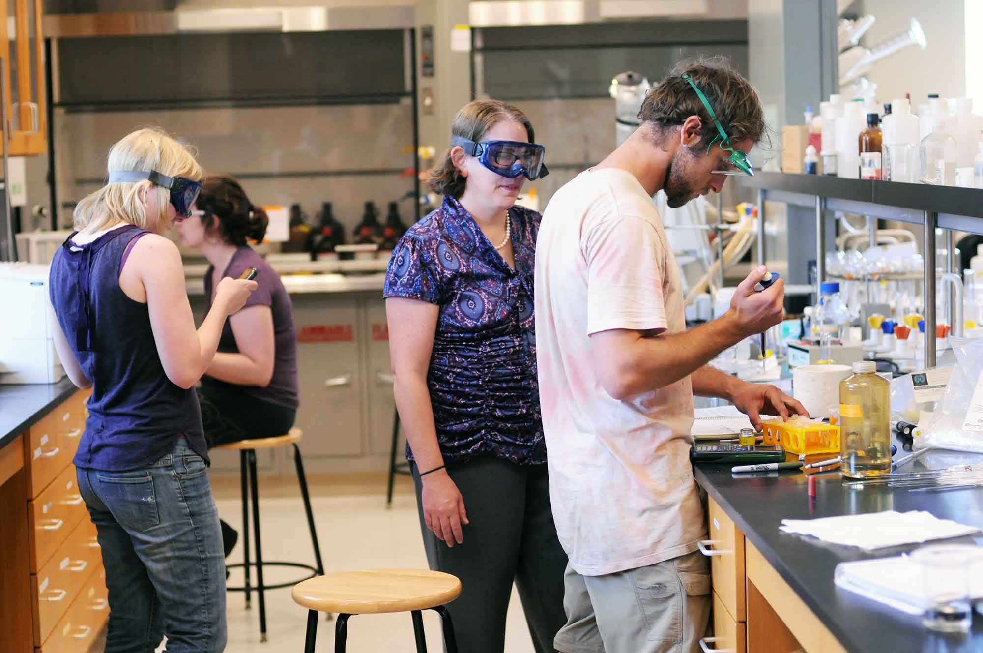 two students work in a lab with a professor 