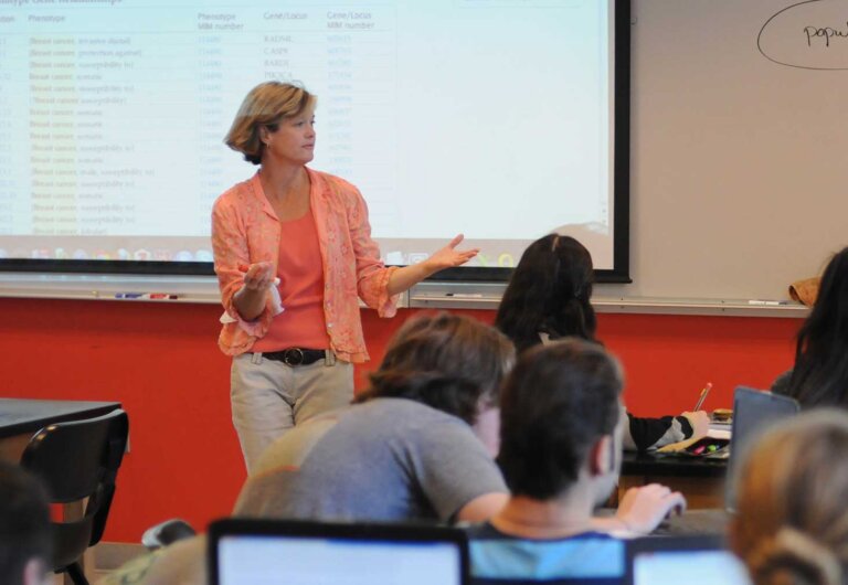 a woman gives a lecture in front of a room full of students.