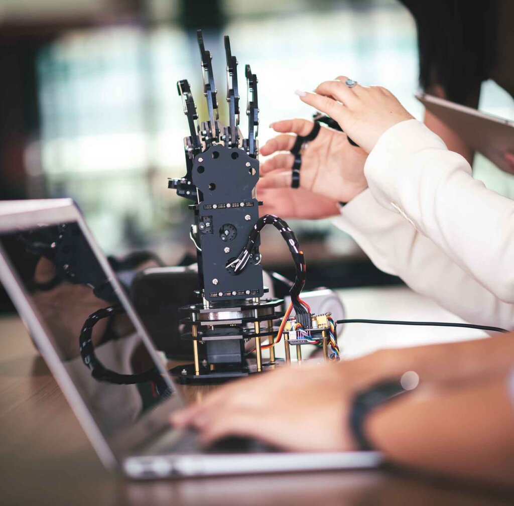 a mechanical hand sits on a desk next to a laptop computer