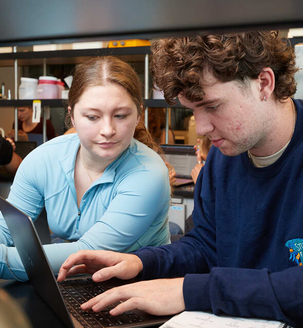 Two students work on a laptop in a cell biology lab