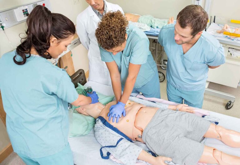 nursing students practice cpr on a dummy while a doctor watches