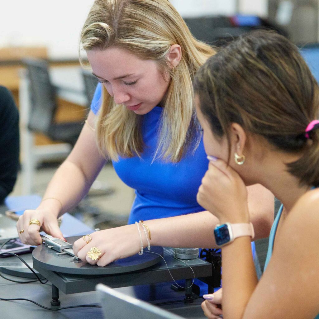 a student works with physics equipment while another student looks on.