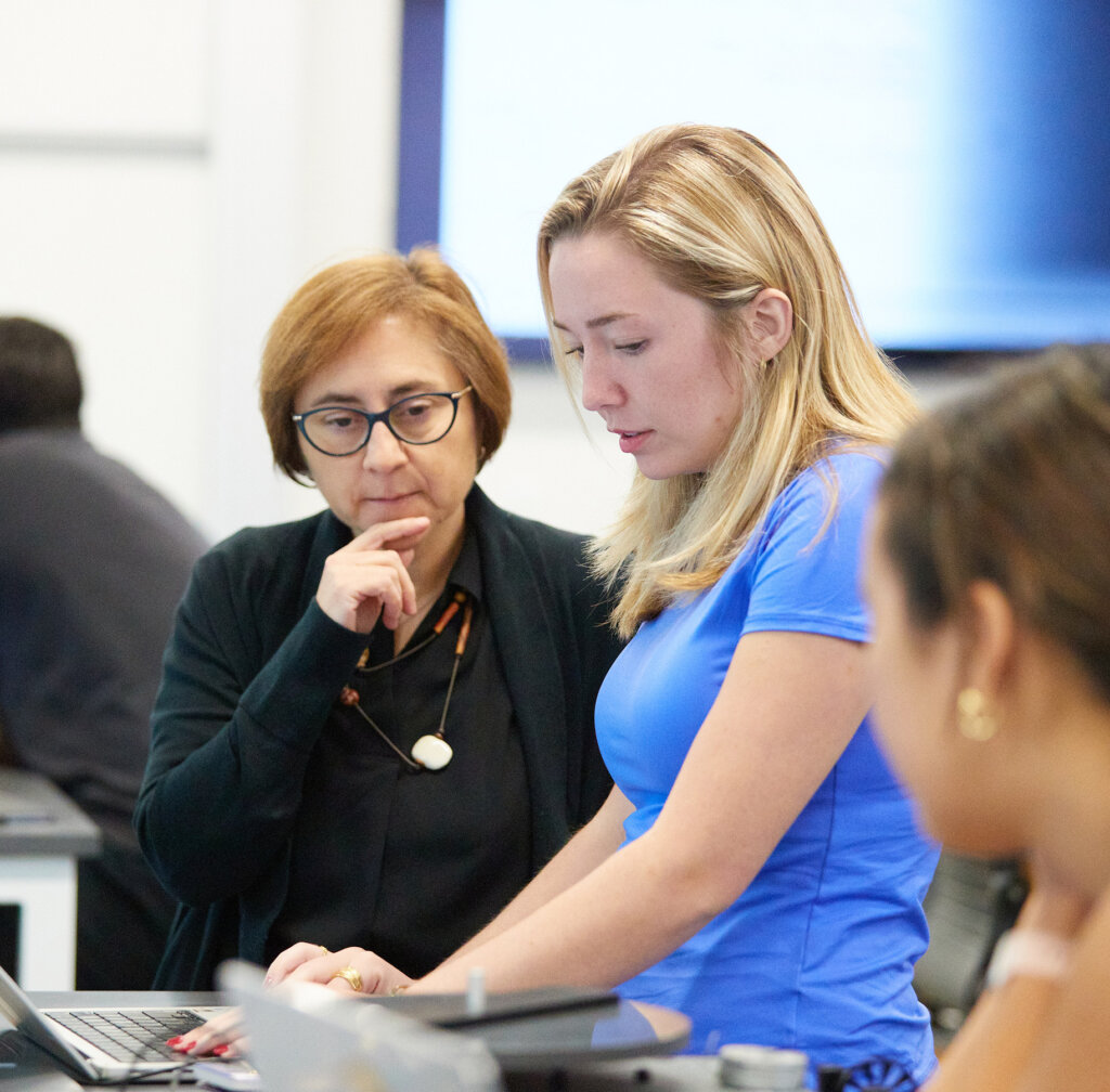 A professor looks on as a student works on a laptop