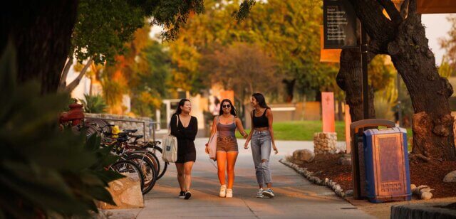 three students in warm-weather clothing walk down a walkway at sunset