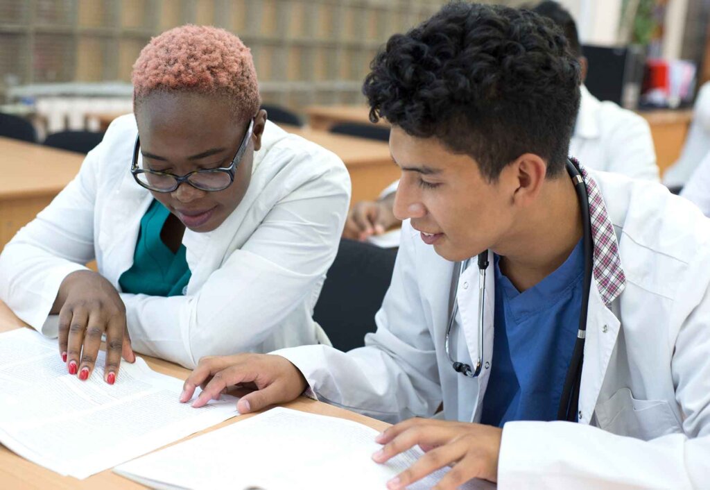 two students in doctors coats review a document.