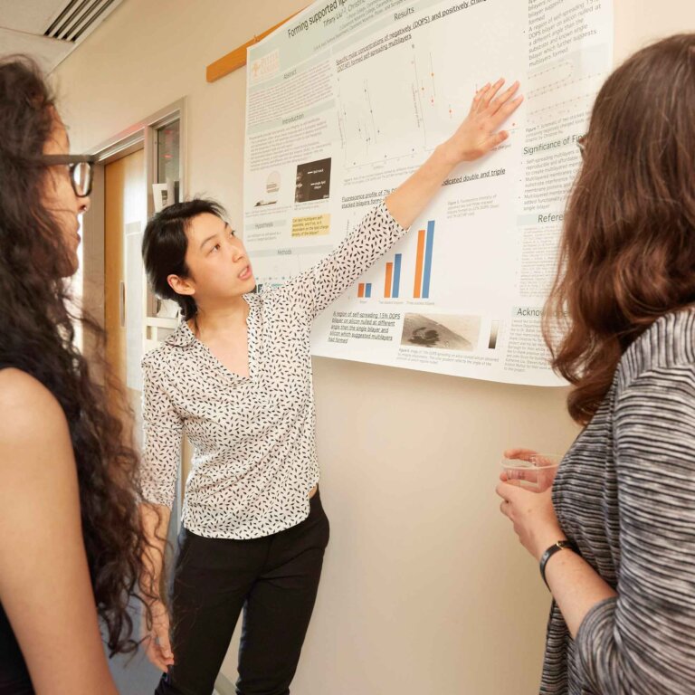 a student presents her research poster to two fellow students