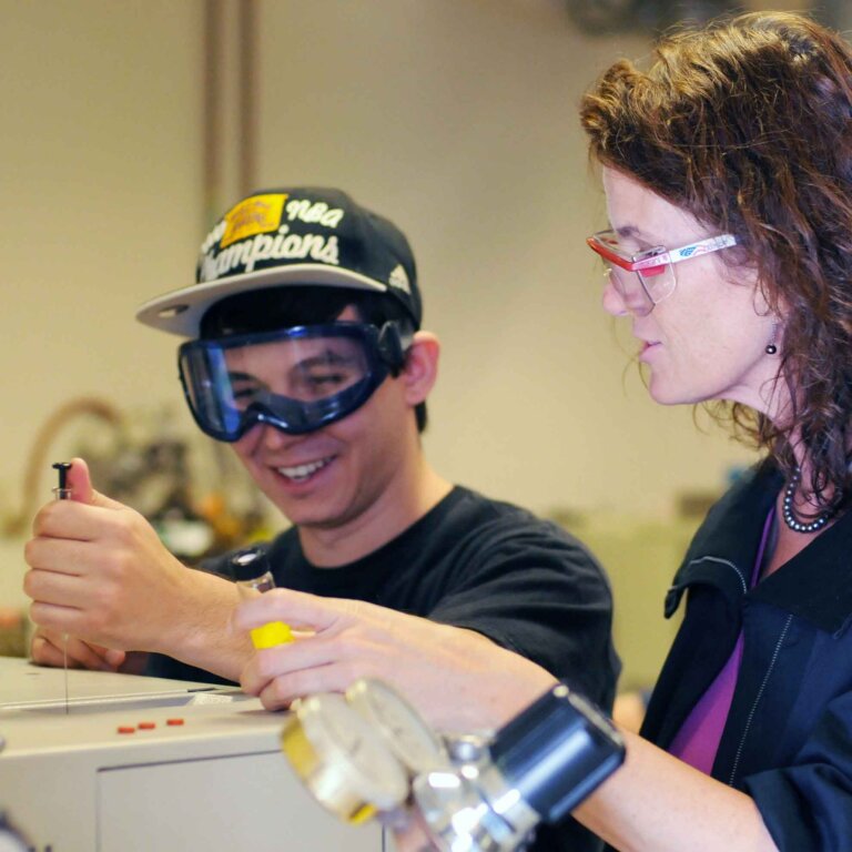 a student works with a syringe with a professor watching