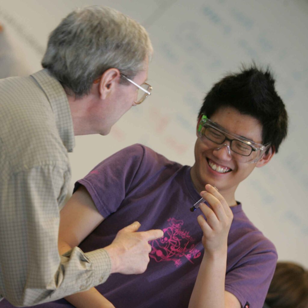 a student laughs with a professor while holding a vial of liquid.