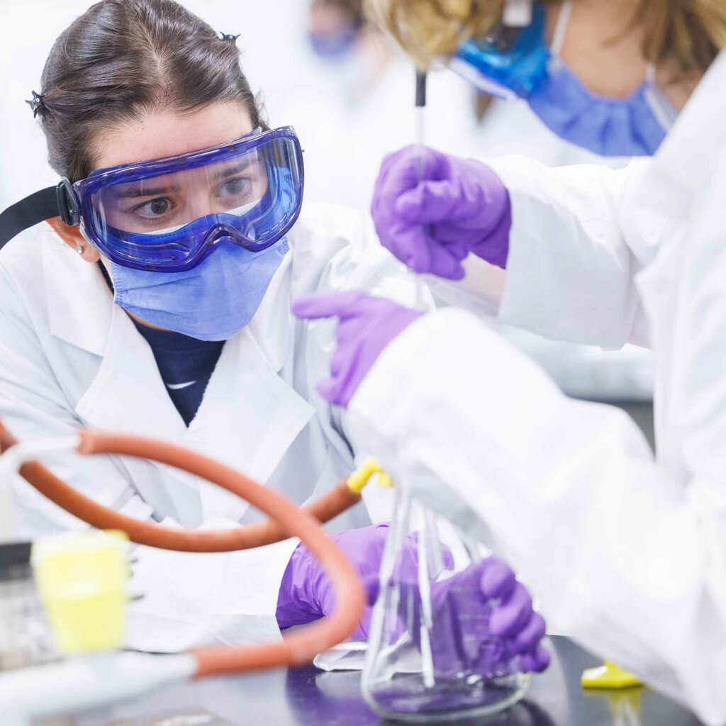 two students wearing protective gear work with chemicals in a lab