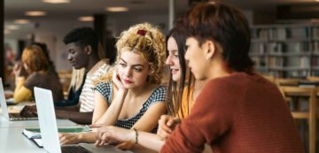 three students work at a laptop together in a library