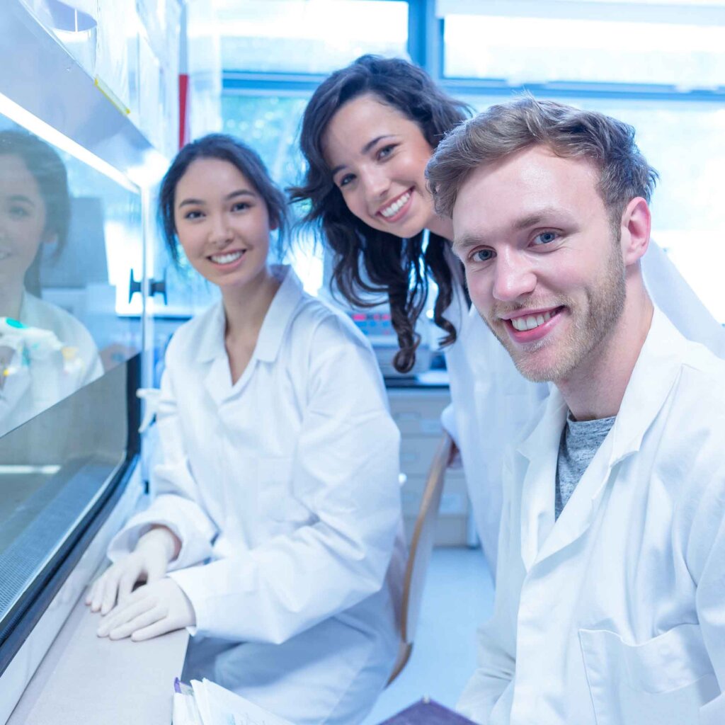 three students in lab coats pose for the camera while smiling