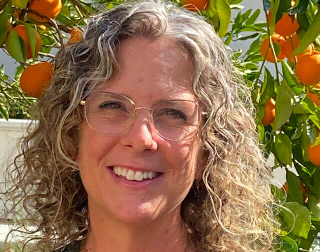 Woman smiling in front of orange tree.